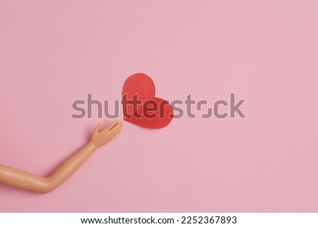 Doll hand with a heart on a pink background. Love concept