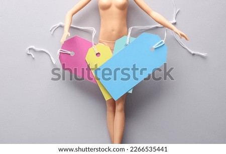 Doll with many empty price tags on a gray background. Sale, shopping concept