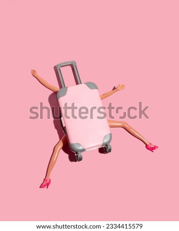 Doll pressed by large suitcase on bright pink background. Funny minimal card travel concept. 