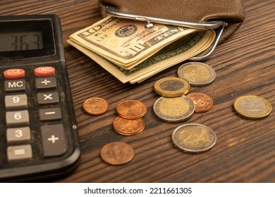 Dollar banknotes, euro coins, a vintage brown leather wallet and a calculator on a wooden surface. Close-up, selective focus. - Powered by Shutterstock