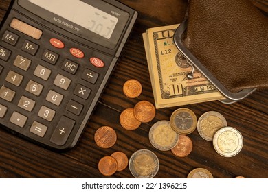 Dollar banknotes, euro coins, a vintage brown leather wallet and a calculator on a wooden surface. Close-up, selective focus. - Powered by Shutterstock