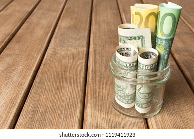 Dollar bills and euros in a glass jar on a wooden table . The concept of poverty .
