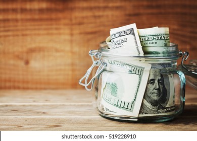 Dollar Bills In Glass Jar On Wooden Background. Saving Money Concept