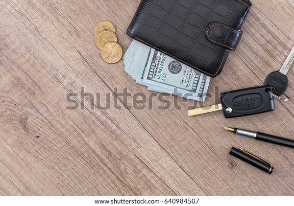 dollar\
cash in wallet and car remote key on wooden\
table.