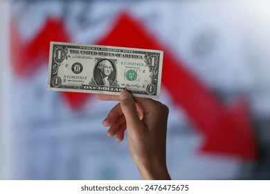 Dollar falling down (the value of the dollar is falling) financial concept. Red arrow indicates decrease of economy and crisis across globe and USA. One dollar hold by woman. 