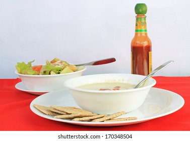 Dollop Of Louisiana Hot Sauce On Bowl Of Broccoli And Potato Soup With Fresh Garden Salad And Saltine Crackers.