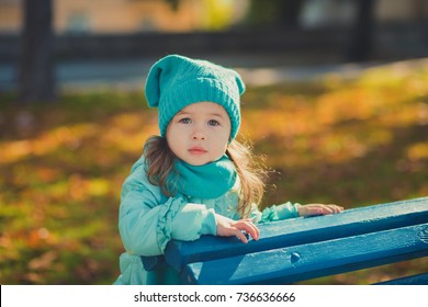 Dolly pin-up toothsome young girl wearing turquoise light blue jacket and warm hat fashion stylish clothes posing in autumn spring park weekend happyly smiling sitting on pathway track