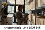 Dolly in portrait shot of cheerful african american warehouse employee scanning cardboard boxes on shelves, updating products labels info before sending parcels to be shipped