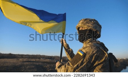 Dolly shot of male soldier in military uniform stands to the peak of hill waving flag of Ukraine. Ukrainian army man lifted blue-yellow banner against blue sky. Resistance to russian invasion concept. Сток-фото © 