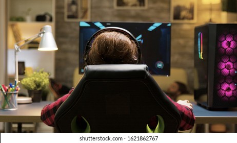 Dolly Shot Of Woman Sitting On Gaming Chair Playing Computer Games. Man Lying On Sofa In The Background.