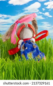 Dolyushka Is A Amulet Slavic Doll Among Green Grass Against Blue Sky. Traditional Homemade Folk Doll Made Of Fabric For Family Happiness And Defender Home.