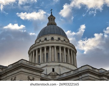 Panthéon Dome Against Dramatic Cloudy Sky - Low-angle close-up of the neoclassical Panthéon's majestic dome and column drum, capped with a cross, set against a dramatically cloudy blue sky.