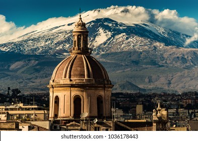 The dome of Cathedral in Catania on the background of volcano Etna in the snow.. The view of the city of Catania with the view of Etna volcano, Sicily, Italy. Catania the UNESCO World Heritage.