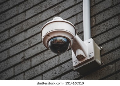 A dome style security camera mounted on a gray brick wall with a conduit box and conduit extending away from the camera towards the top of the image.