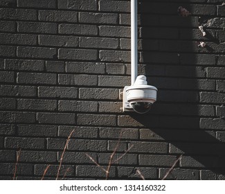 A dome style security camera mounted on a gray brick wall with a conduit box and conduit extending away from the camera towards the top of the image.