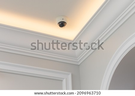 Dome surveillance video camera mounted on the ceiling of the classic design room with moldings and ceiling skirting