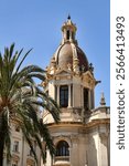 A domed section of Valencia City Hall, with intricate architecture, ornate columns, and a red-tiled dome. A palm tree adds a Mediterranean vibe under the clear blue sky.
