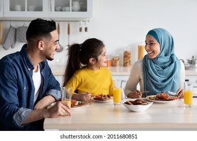 Domestic Breakfast. Happy Middle Eastern Family Of Three Eating Together In Kitchen, Cheerful Young Arab Parents And Little Daughter Sitting At Table, Enjoying Tasty Food, Chatting And Laughing