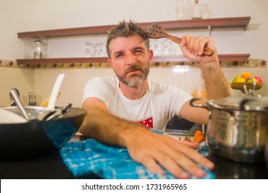 Domestic Chores Stress - Young Attractive Overworked And Depressed Man In Red Apron At Home Kitchen Feeling Stressed And Tired Of Cooking And Dishwashing In Frustrated Face Expression