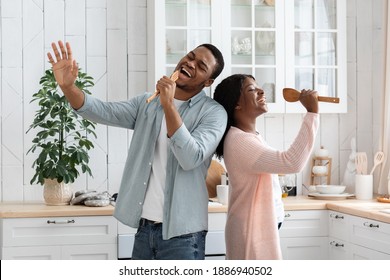 Domestic Concert. Playful African American Couple Having Fun In Kitchen, Singing And Dancing While Cooking Lunch At Home, Cheerful Black Millennial Spouses Using Spatulas As Microphones, Free Space - Powered by Shutterstock