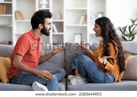 Domestic Conflicts. Portrait Of Young Indian Couple Arguing At Home, Millennial Eastern Spouses Suffering Relationship Problems And Misunderstanding, Sitting On Couch And Quarreling With Each Other