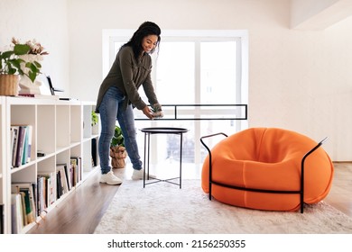 Domestic Decor. Smiling Young Black Woman Putting Vase With Plant On Tea Coffee Table. Casual Interior Designer Taking Care Of Coziness In Stylish Apartment Creating Atmosphere Moving In New House