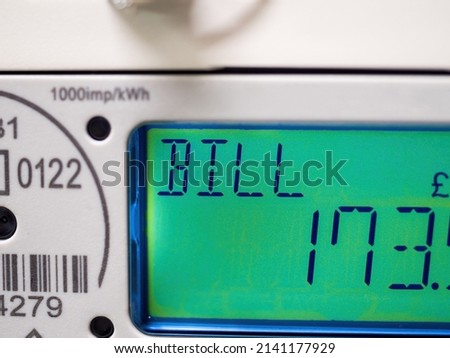 A domestic electric smart meter close-up. Green LCD display shows current bill. Concept for energy bills, price rise, inflation, cost of living and meter reading. Windfall tax.