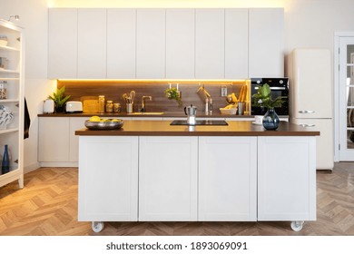 Domestic Life And Household Equipment Concept. Front View Of Contemporary Interior With White Kitchen Cupboards, Wooden Countertop, Geyser Coffee Maker On Ceramic Glass Stove Against Electric Oven