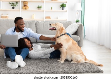 Domestic Life. Portrait Of Happy Couple Spending Time Together At Home In Living Room, Guy Using Computer And Stroking Labrador, Woman Lying On Boyfriend's Lap And Playing With Dog