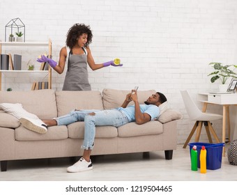 Domestic Life Problem. Angry African-american Woman Shouting At Her Lazy Boyfriend, Guy Is Using Smartphone And Using Smartphone, Ignoring Her, Copy Space