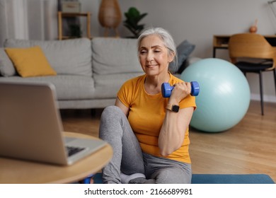 Domestic Online Sports Training. Senior Woman Doing Exercises With Dumbbells In Front Of Laptop In Living Room. Fit Mature Lady Working On Her Arm Muscles, Following Video Tutorial