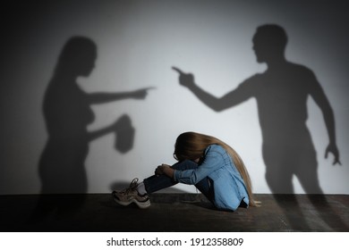 Domestic physical violence, abusing. Scared little caucasian girl, victim sitting close to white wall with shadow of angry threatening parents with alcohol addiction. Awareness of social problem.