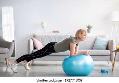 Domestic Sports During Covid-19 Concept. Athletic Mature Woman Standing In Plank On Fitness Ball, Working Out Core Muscles At Home. Strong Senior Lady Doing Abs Exercise Indoors