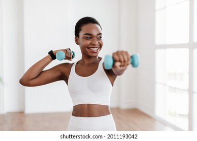 Domestic Training With Weights  Positive black lady doing exercises and dumbbells  strengthening her body at home  Smiling young female in braces working her biceps muscles  staying healthy