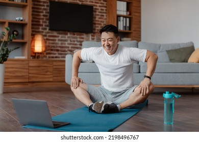 Domestic Trainings Concept. Mature Asian Man Practicing Yoga With Online Instructor On Laptop, Making Butterfly Asana, Watching Sports Tutorial, Training At Home