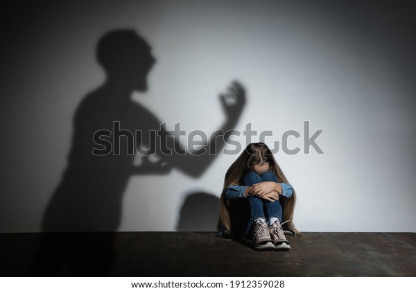 Domestic violence, abusing. Scared little\
caucasian girl, victim sitting close to white wall with shadow of\
angry father\'s threatening on it. Awareness of social problem,\
childhood, physical\
violence.