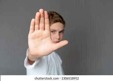 Domestic violence and child abuse. Boy showing stop gesture with his hand, gray background