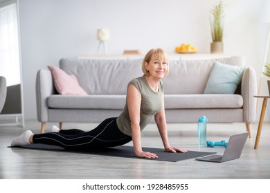 Domestic yoga practice. Flexible mature woman doing cobra pose on mat, following online sports video at home, copy space. Senior lady exercising, keeping in perfect shape during covid quarantine