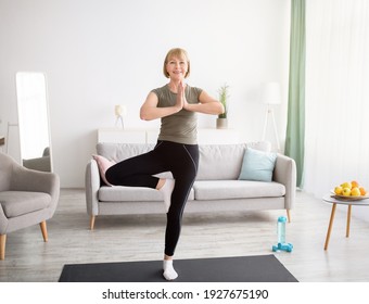 Domestic yoga practice. Positive mature lady standing in tree pose, keeping balanced during covid lockdown at home. Happy senior lady in sportswear exercising indoors, copy space