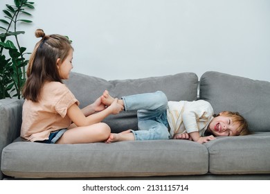 Dominant little girl tickling to tickle boy's foot, making him roll and laugh. On the couch side view.