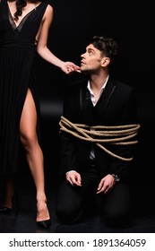 Dominant Woman In Dress Standing And Touching Face Of Tied Submissive Man On Black