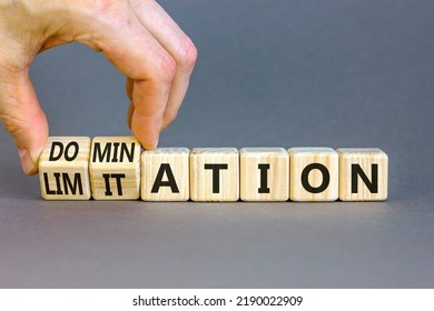 Domination or limitation symbol. Businessman turns cubes, changes the word domination to limitation. Beautiful grey table, grey background, copy space. Business, domination or limitation concept.