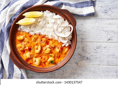 Dominican Cuisine: Shrimps In Coconut Milk Sauce With Coconut Chips, Served With Rice, In A Clay Pot On A White Wooden Table Framed By Kitchen Dish Towel With Blue Stripes, Copy Space, Top View