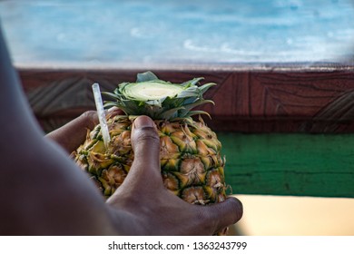 Dominican Man's Hand Holding A Pina Colada Cocktail Served In The Pineapple, In A Tropical Beach In The Dominican Republic. Vacation Concept.