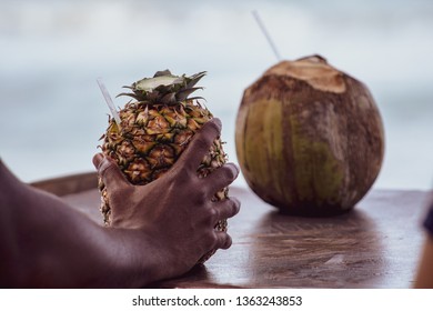 Dominican Man's Hand Holding A Pina Colada Cocktail Served In The Pineapple, In A Tropical Beach In The Dominican Republic. Vacation Concept.