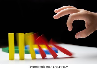 Domino Effect. Domino Of Colorful Wooden Blocks. Children's Hand Pushes Dominoes On A White Table. Motion Effect