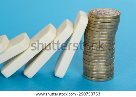 Domino Falling On Stack Of Euro Coins Over Blue Background