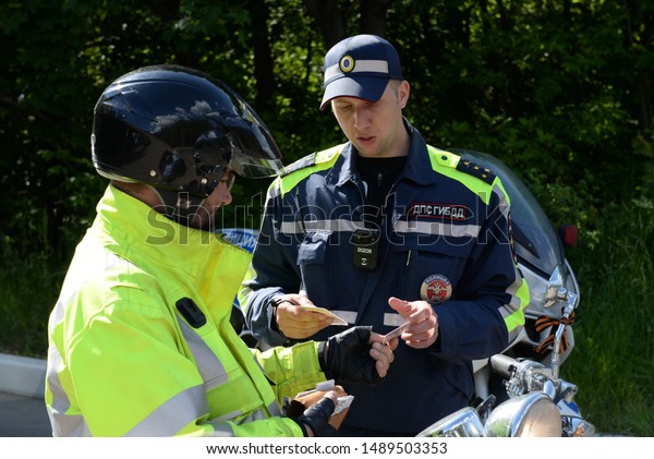 DOMODEDOVO, MOSCOW REGION, RUSSIA - JUNE 1,\
2019:The inspector of road patrol service of police checks\
documents at the driver of a\
motorcycle