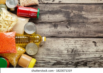 Donate Food Delivery Concept For Senior Elderly In Covid Quarantine By Volunteer. Donations Food Set Of Staple Products Raw Cereals Canned Food, Grocery Pasta On Wooden Table. Flat Lay Copy Space