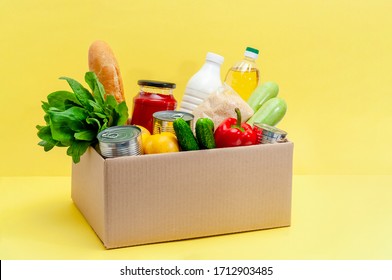 Donation Box with Supplies Food for People in Isolation on Yellow Background. Essential Goods: Oil, Canned Food, Cereals, Milk, Vegetables, Fruit